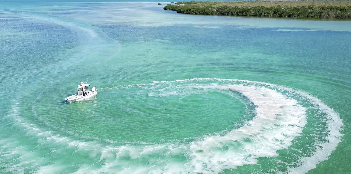 Aerial view of a fishing boat turning through shallow turquoise water at Miss O Sportfishing