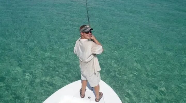 Angler casting from the bow of a skiff over clear turquoise water