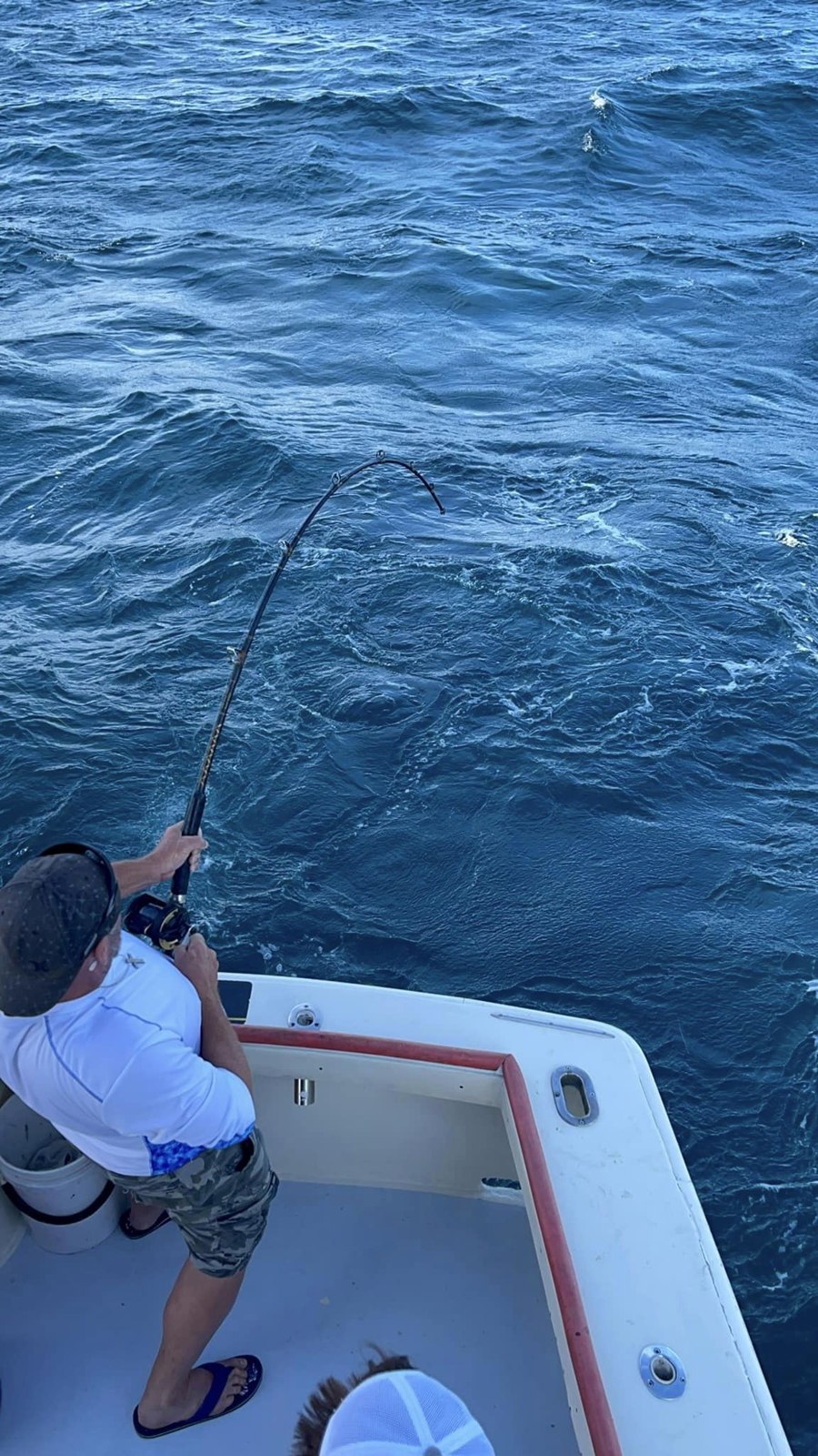 Angler fishing from a boat’s stern above blue offshore water