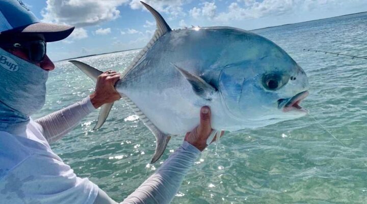 Angler holding a permit beside a skiff with Florida Keys Flats Fishing