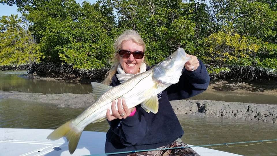 Angler holding a snook beside mangroves with Captain Ted Wilson