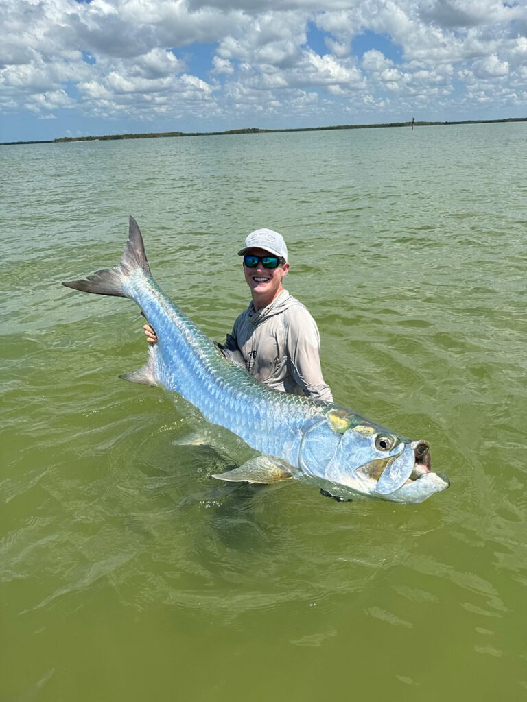 Angler standing in shallow water beside a tarpon with 10K Charters