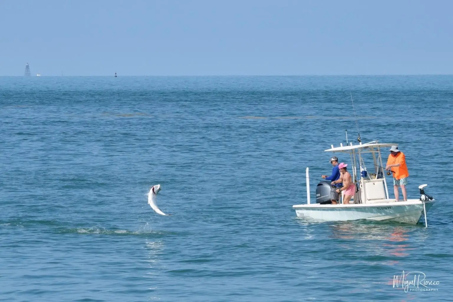 Anglers aboard a flats boat with a fish jumping nearby with ShadowCaster Charters