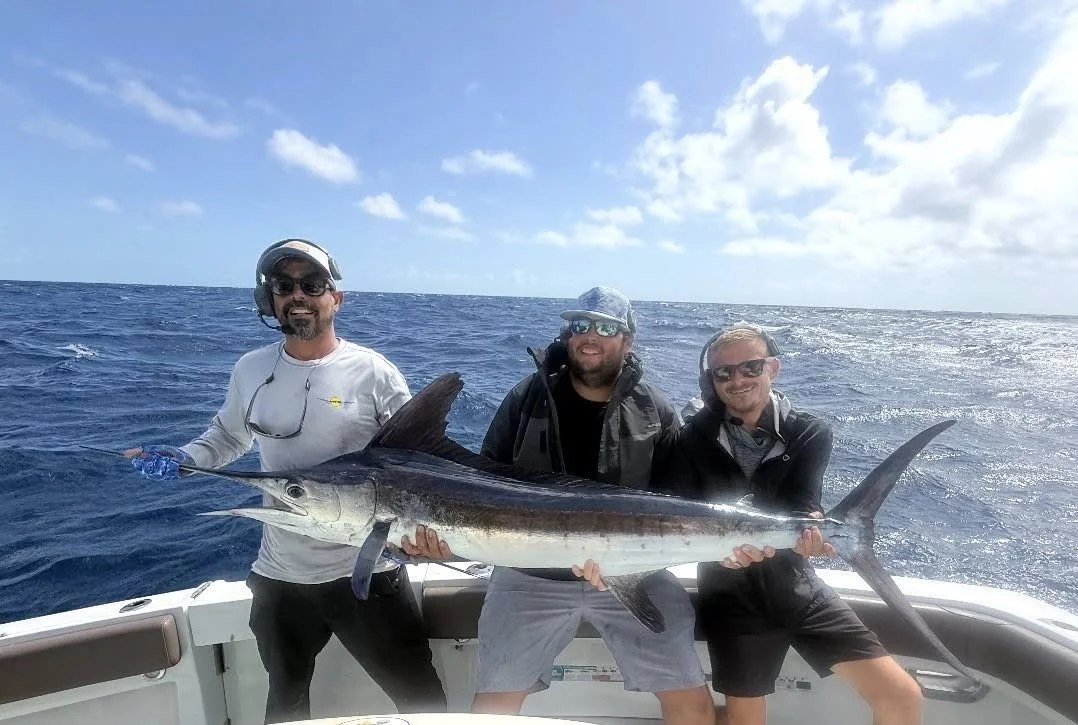 Anglers displaying a long silver fish aboard Atlantic and Gulf Fishing Charters