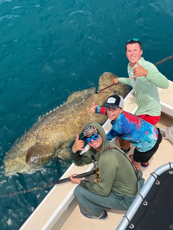 Aqua Delights anglers holding a large grouper beside the boat
