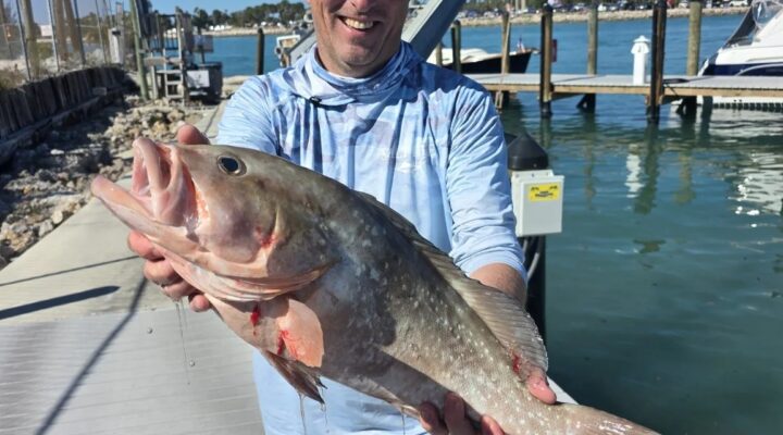 Aquaholic Charters angler holding a grouper beside a marina