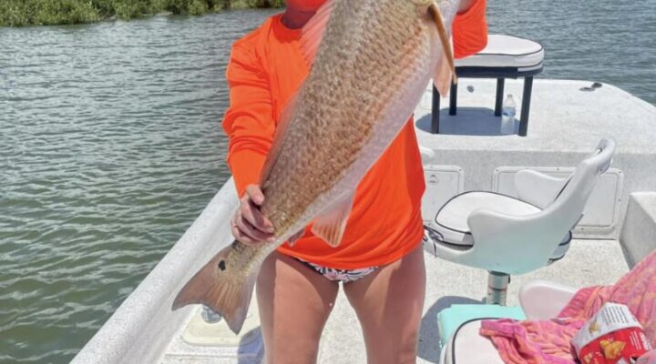 Captain Ray's Fishing Charter angler holding a redfish beside the boat