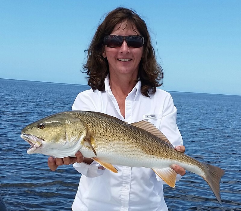 Crystal Sea Charters guest holding a redfish beside open water