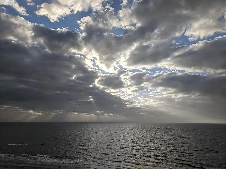 Sunlight breaking through clouds over the water at Indian Shores