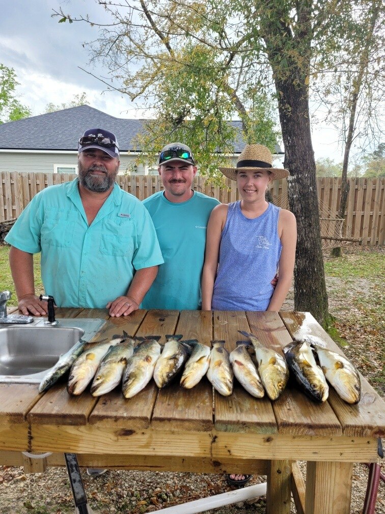 Three Shell Yeah guests posing behind fish on a cleaning table