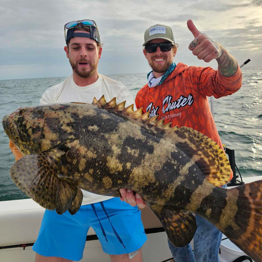 Two anglers holding a grouper on a Six Chuter Charters boat