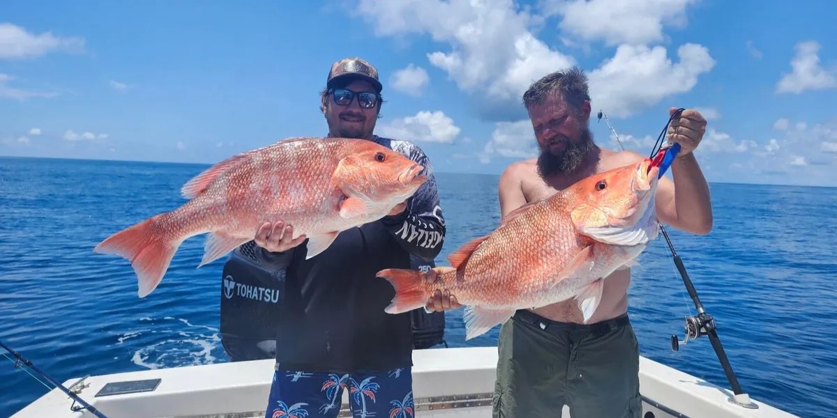Two Captain Harvey charter guests holding large red fish offshore