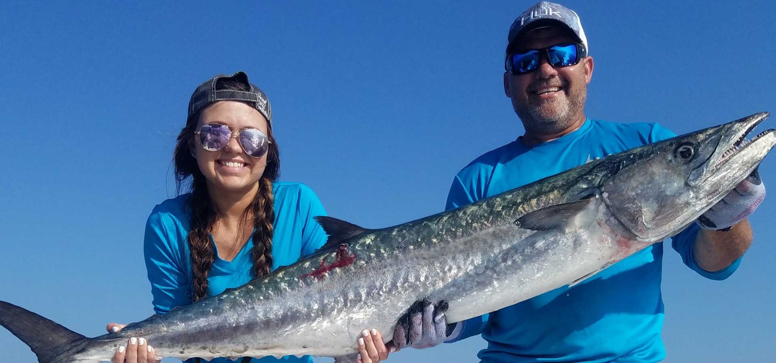 Two Hammerhead Hunters guests holding a long silver fish aboard a boat