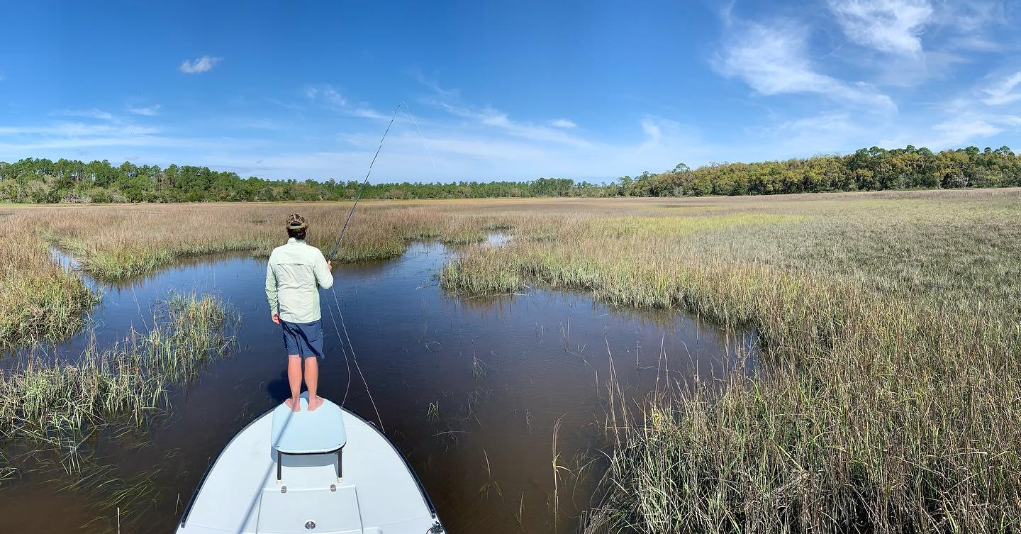 Amelia On Fly angler casting from a skiff into a flooded marsh