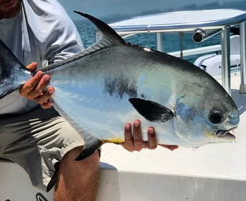 Angler holding a permit aboard a Hot Water Fishing skiff