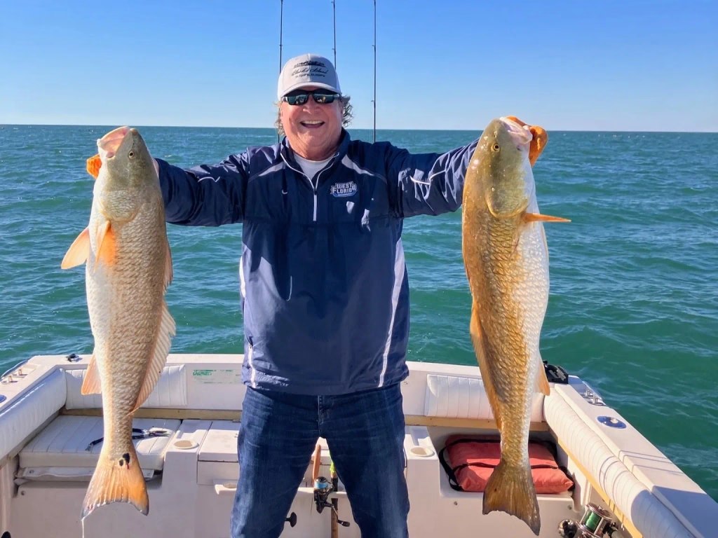 Angler holding two redfish on an Its A Good Day fishing trip