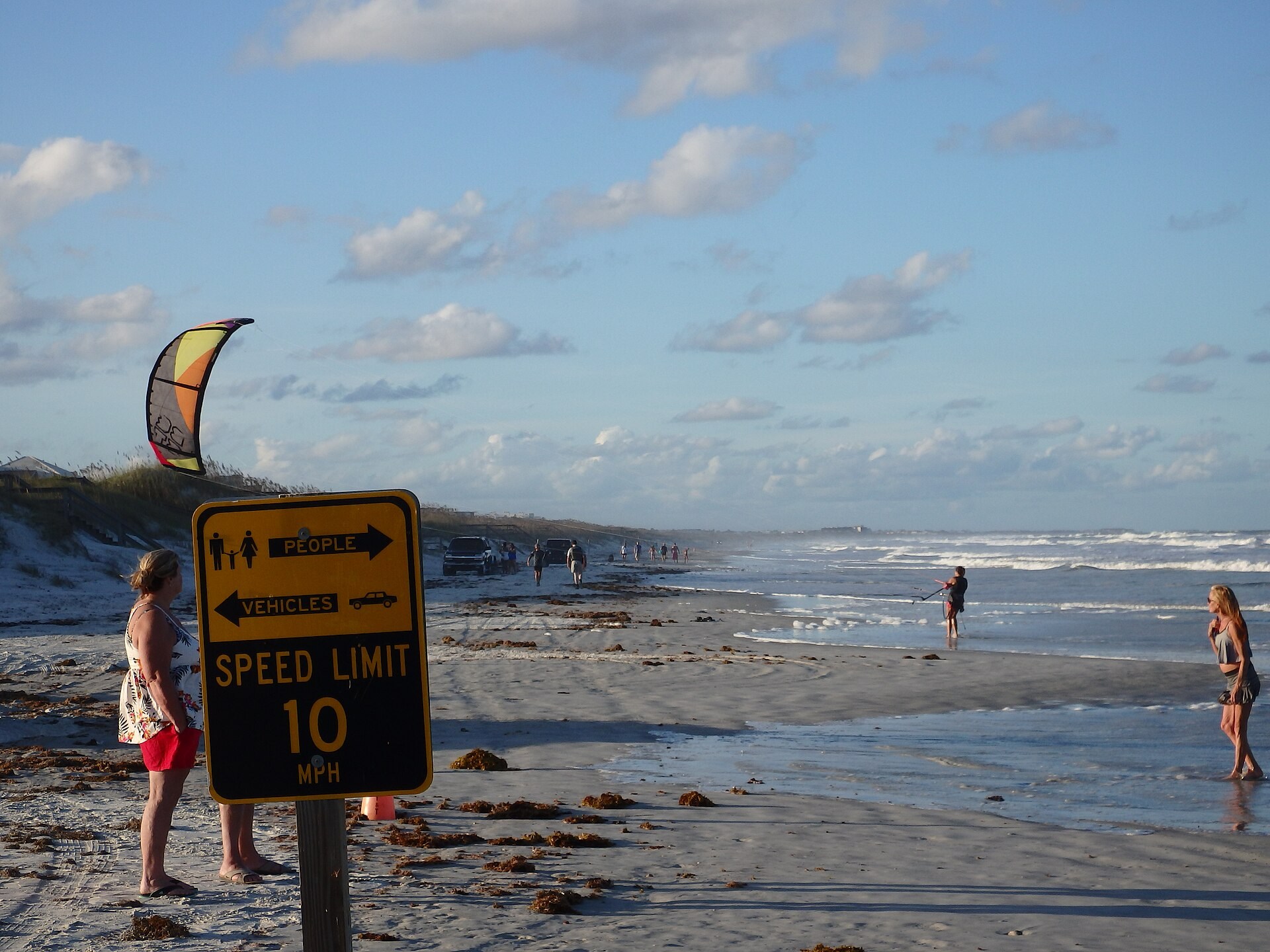 Crescent Beach shoreline with surf, beachgoers and a vehicle speed sign