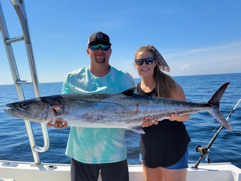 Dawn Patrol anglers holding a king mackerel beside the boat tower