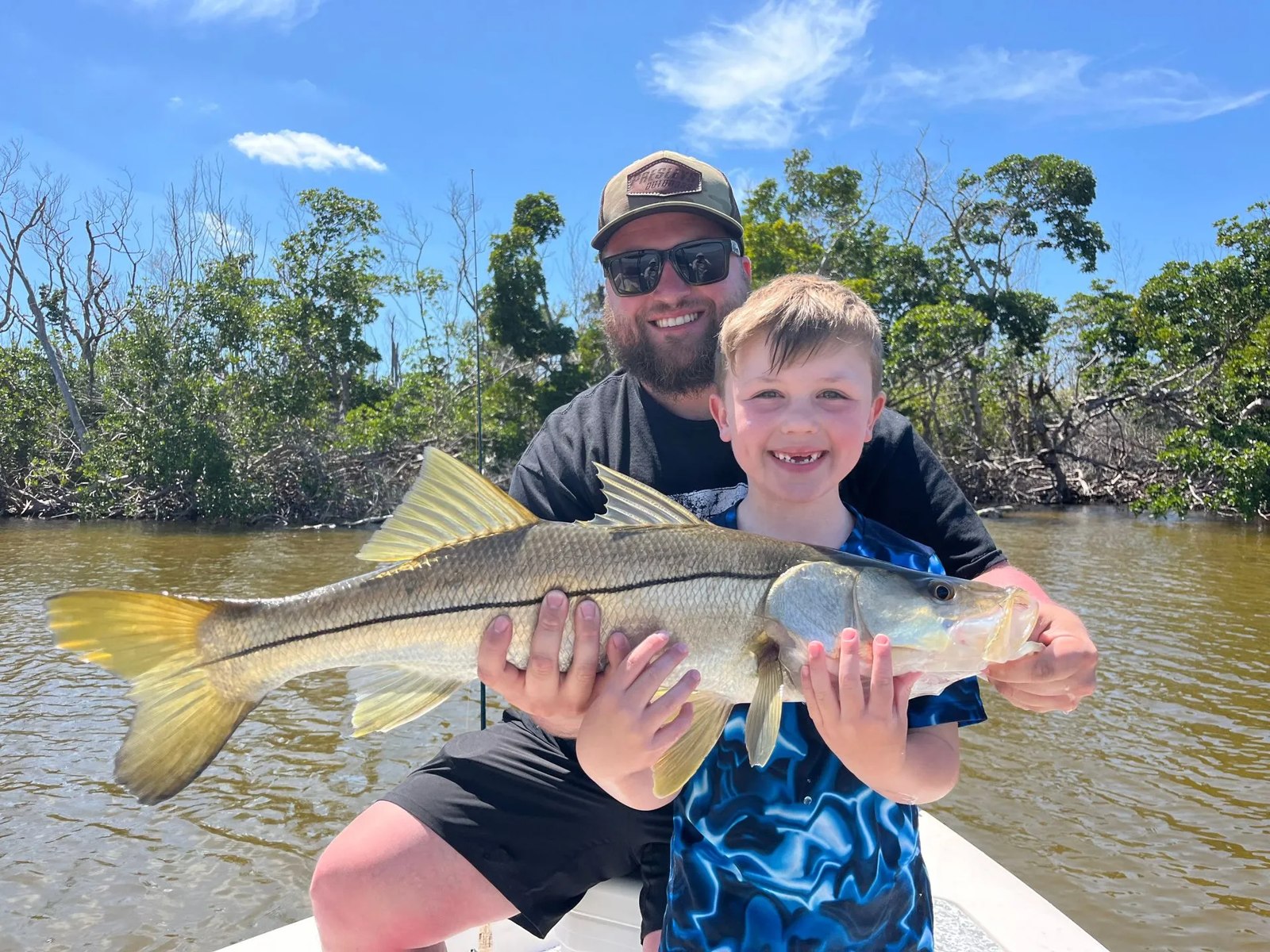 Guide helping a child hold a snook on an All In fishing outing