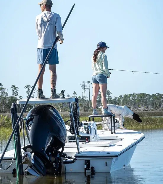 Guide poling a skiff while an angler casts on a Redwater outing