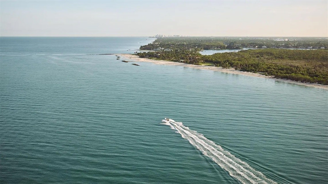 Boat passing Keewaydin Island beside its sandy shoreline