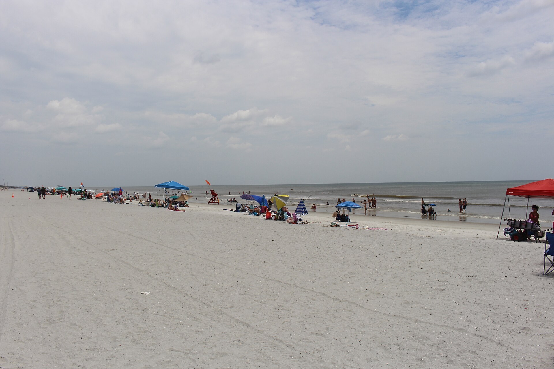 Beachgoers and tents along Neptune Beach beneath a cloudy sky