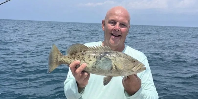 Salt Bird Charters angler holding a grouper over Gulf water