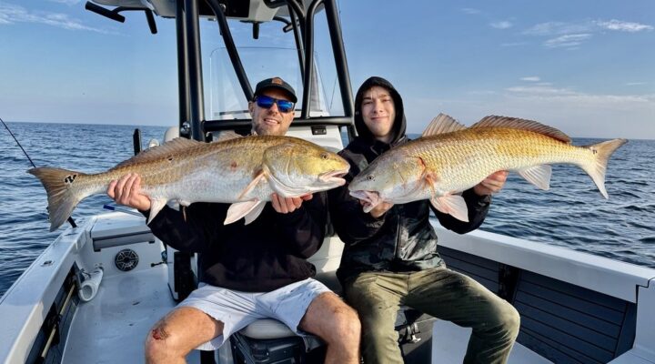 Two anglers holding redfish aboard a Coastal Fish charter